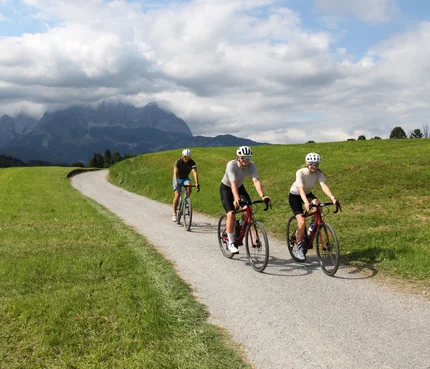 Brixental © Michael Küchl Drei Radfahrer auf Landstraße mit Bergen und Wolken im Hintergrund