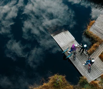 NOCKBIKE Area © Martin Hofmann Drei Radfahrer auf einem Steg am See mit Wolkenreflektion im Wasser