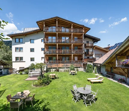 Sporthotel Exclusive © Sporthotel Exclusive SAS Großer Garten mit Tischen, Stühlen und Liegestühlen vor Alpenhaus