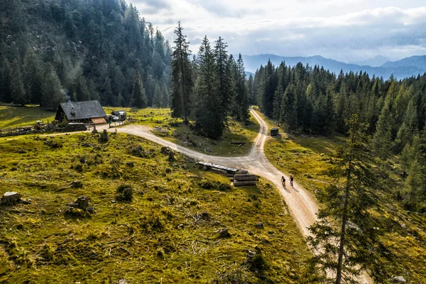 Gravelbike Holidays © WOM Medien GMBH - Andreas Meyer Two cyclists on a trail in forested mountain area near a cabin