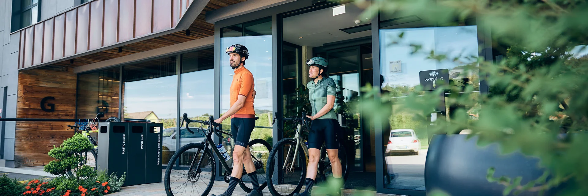 Gravelbike Holidays © Tobias Köhler Two cyclists in sportswear walking with their bikes out of a modern building