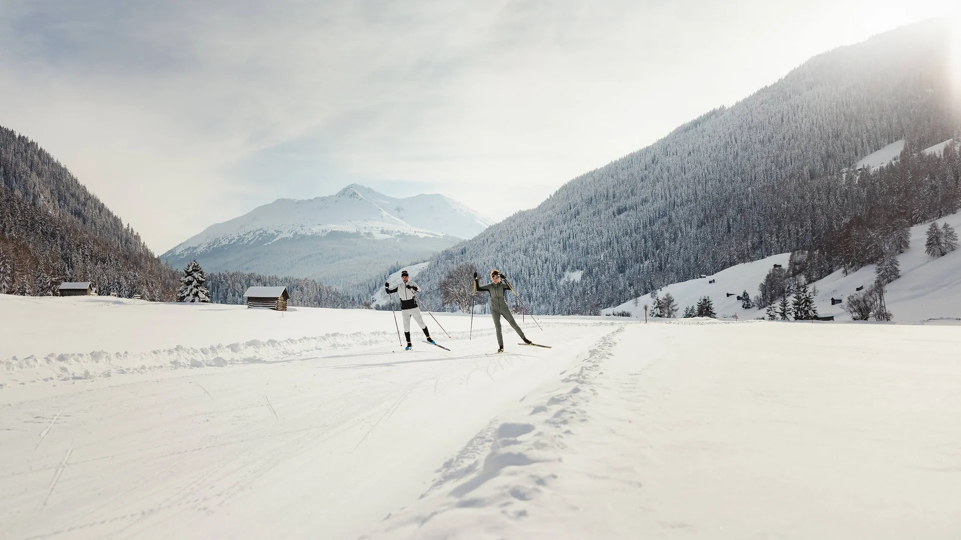 Cross-country skiing & ski touring hotel © Alex Moling Two cross-country skiers on a snowy trail with forested mountains and sunlight