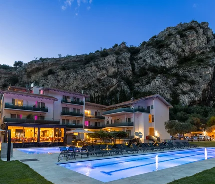 Triathlon & Gravel Aktivhotel SantaLucia © Fabio Staropoli Hotel mit beleuchtetem Pool vor Felsklippe bei Abenddämmerung