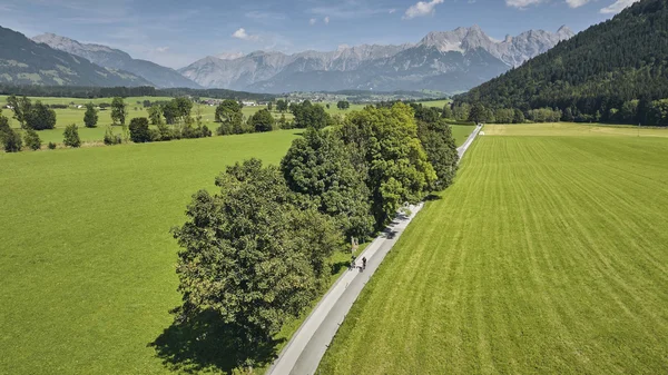 Velontour © TVB Maishofen Cyclists on country road lined with trees and mountains in the distance