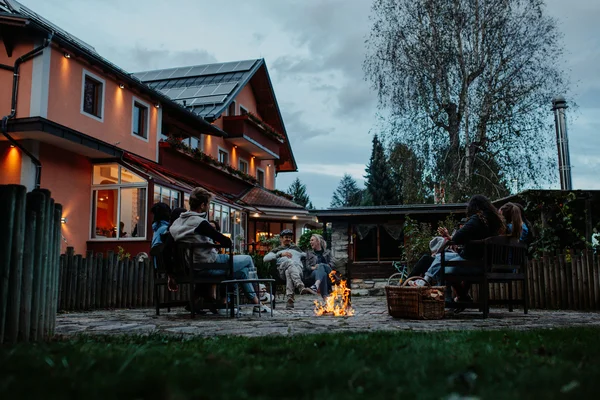 Group of people sitting around a fire pit in a backyard during evening