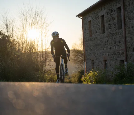 Toskana © Tenuta il Cicalino Radfahrer in schwarzer Kleidung fährt auf Landstraße bei Sonnenuntergang