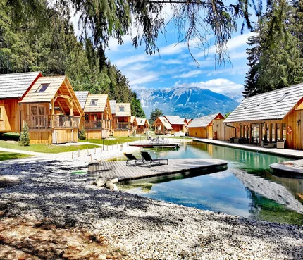 Hotel & Glamping Ribno Alpine Resort © Katarina Strgar Holzhütten am See mit Bergblick und Liegestühlen auf Holzsteg