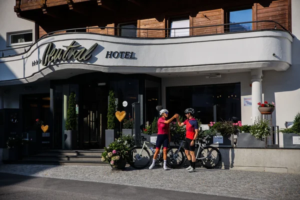 Two cyclists fist bump in front of Central Hotel