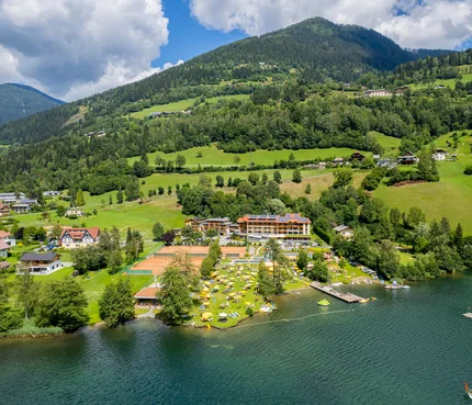 Familien- & Sportresort Brennseehof © Gert Perauer Seeufer mit Strand, Liegestühlen und Tennisplätzen vor bewaldeten Bergen
