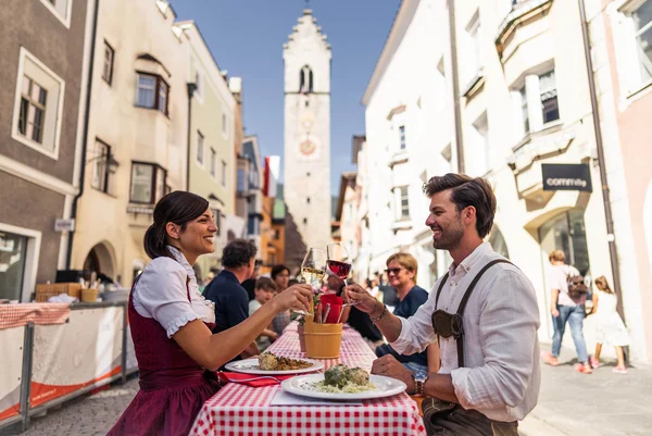 Couple clinking wine glasses while dining at an outdoor table in old town
