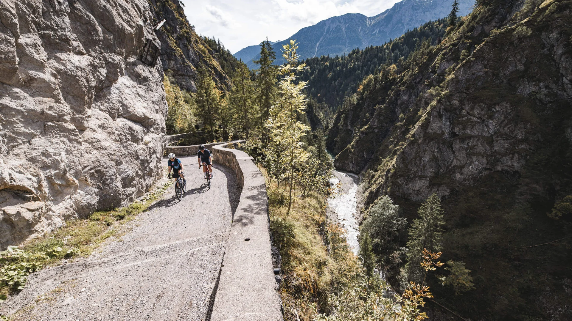 Gravelbike Holidays © Andreas Vigl Two cyclists on mountain trail beside river in forested canyon