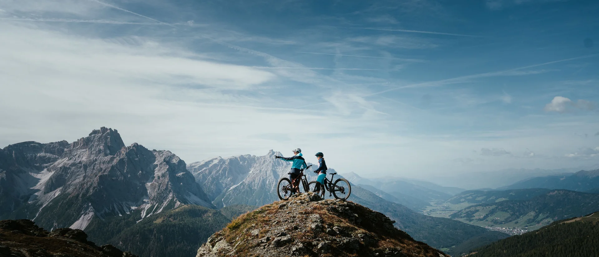 Two mountain bikers on a peak overlooking mountain range