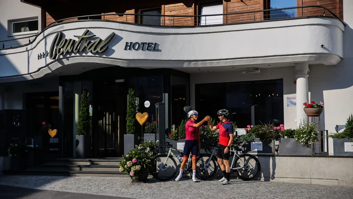 Projects & Case Studies © Felix Saller Two cyclists high five outside a hotel with flower arrangements.