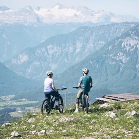 Zwei Radfahrer stehen auf Wiese mit Blick auf Berge