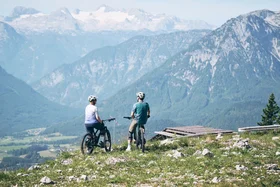 Two cyclists standing on grassy hill overlooking mountains