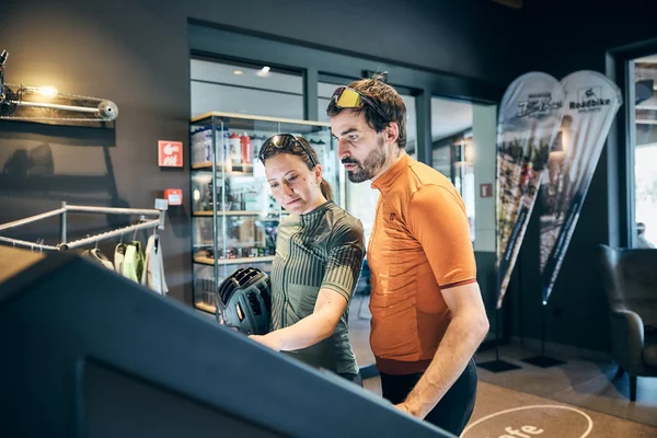 Two cyclists in sportswear looking at a screen inside a shop