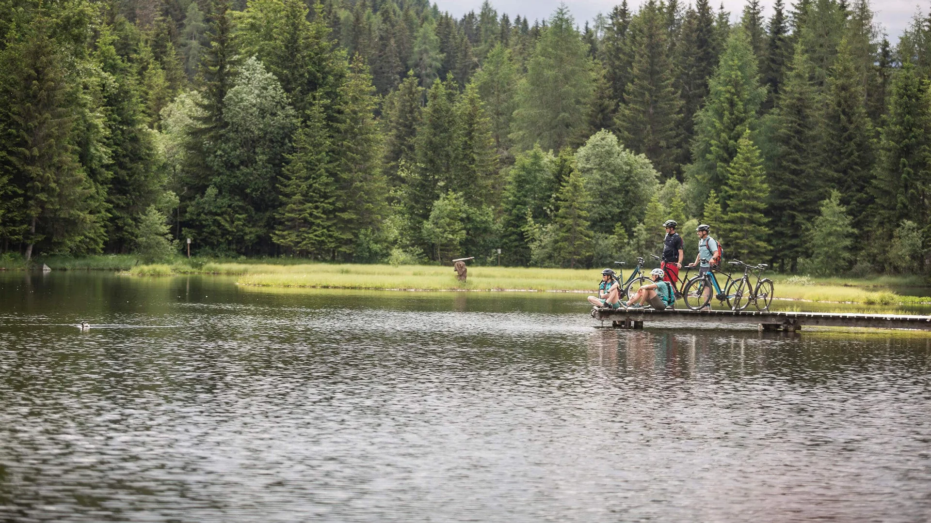 Velontour Cyclists on a pier by a lake in a forested area