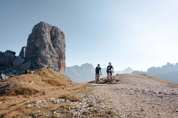 Gravelbike Holidays © Josef Plaickner Two cyclists on mountain trail with large rock formation and mountain backdrop