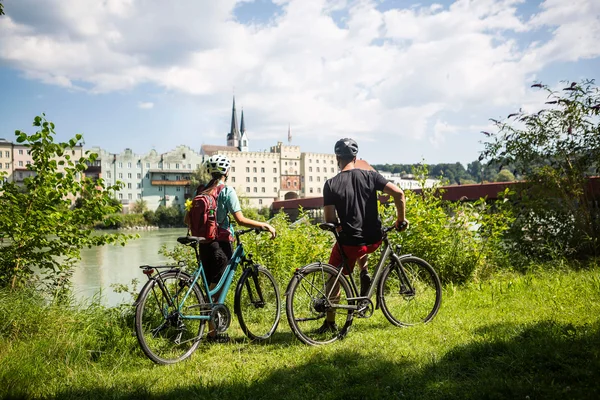 Velontour © Velontour Two cyclists wearing helmets overlooking riverside buildings on a sunny day