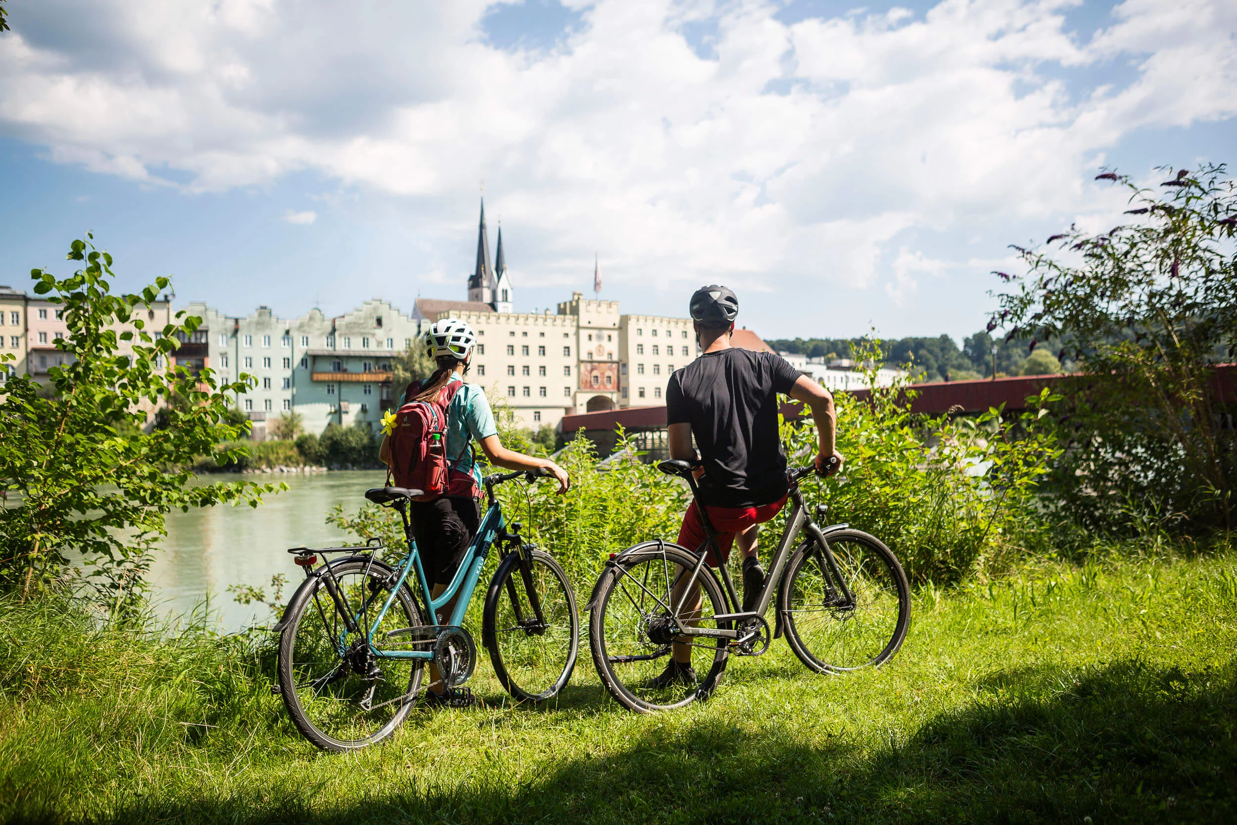 Two cyclists wearing helmets overlooking riverside buildings on a sunny day
