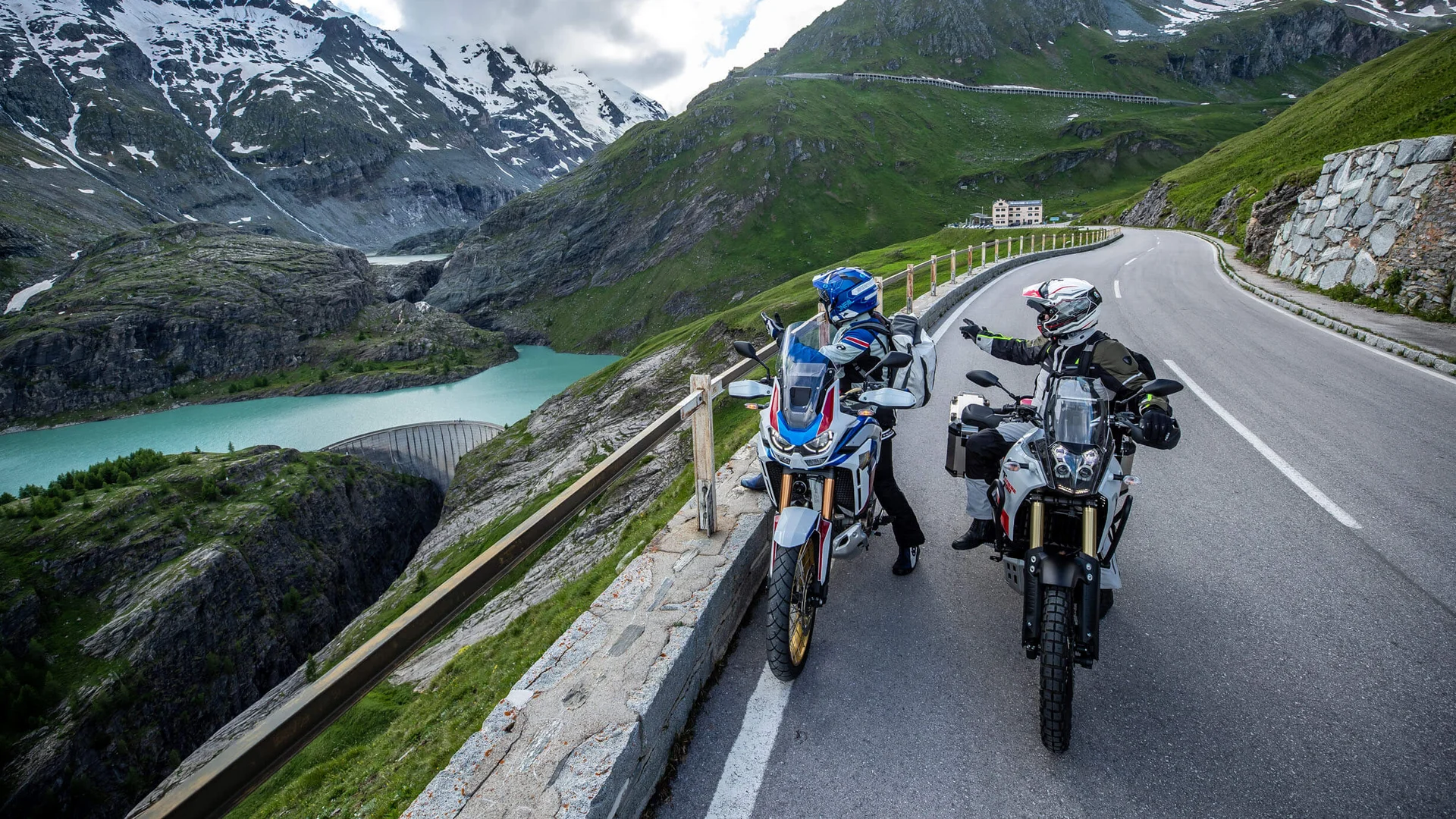 MTS Austria © Arturo Rivas Two motorcyclists on alpine road with mountain lake and snowy peaks