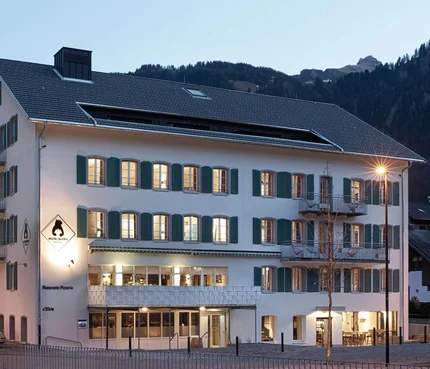 Hotel Bären & Cafe Deli © Hotel Bären - Cafe Deli Mellau Hotelgebäude mit beleuchteten Fenstern am Abend in bergiger Umgebung
