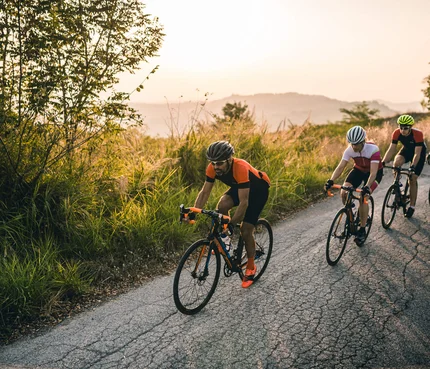 Emilia Romagna © Alex Moling Vier Radfahrer fahren auf einer Straße neben grüner Vegetation am Abend
