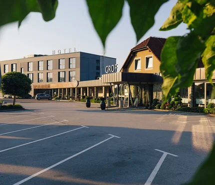 Hotel Grof © Ziga Intihar Hotelgebäude mit Parkplatz, teilweise eingerahmt von grünen Blättern bei Sonnenuntergang