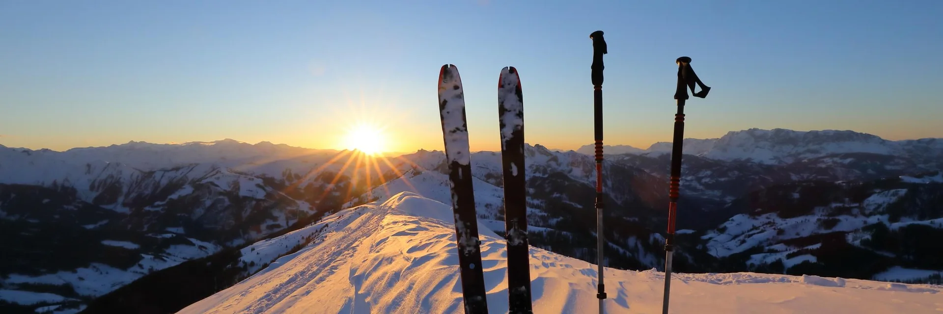 Skis and poles in snow at sunset on a mountain peak