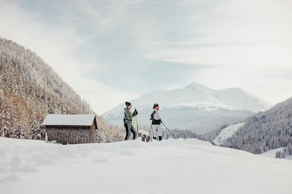 Destination development © Alex Moling Two people cross-country skiing in snowy mountain valley with huts in background