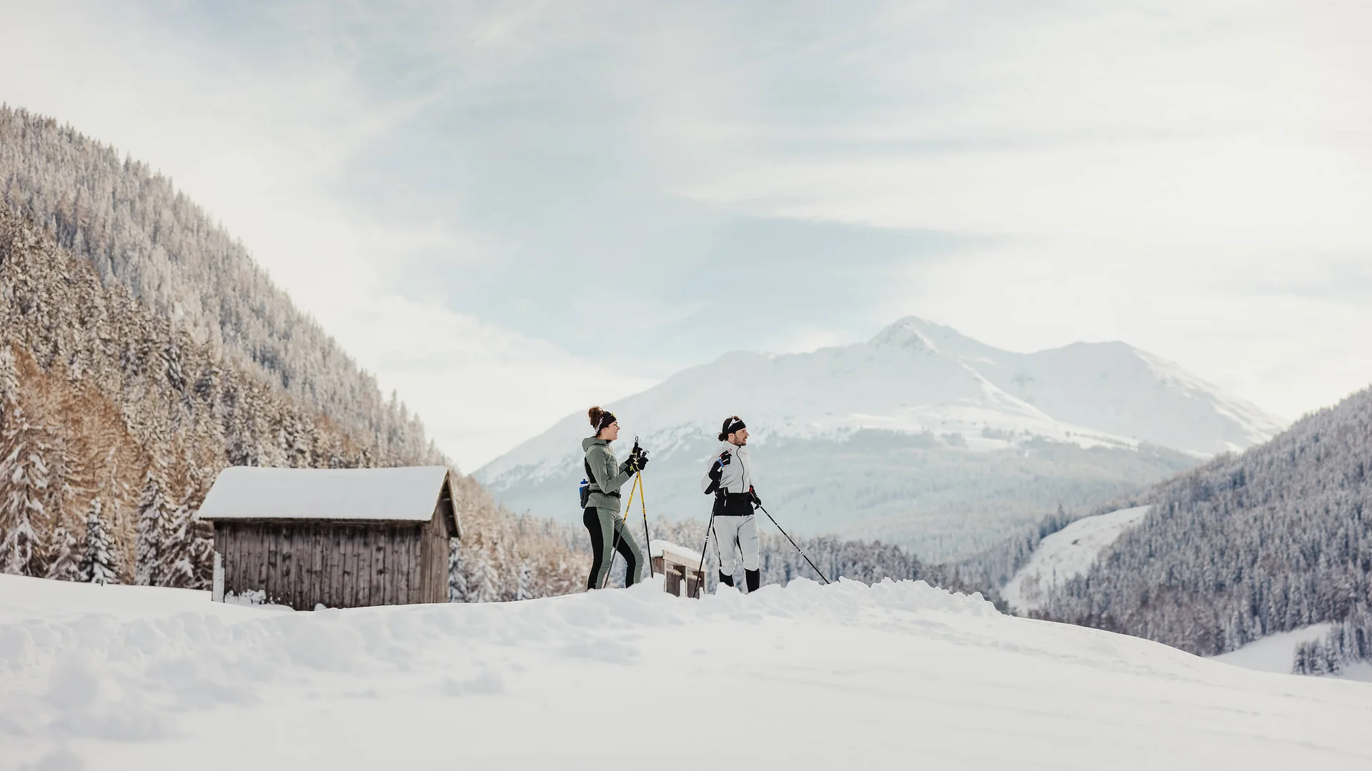 MTS Austria © Alex Moling Two people cross-country skiing in snowy mountain valley with huts in background