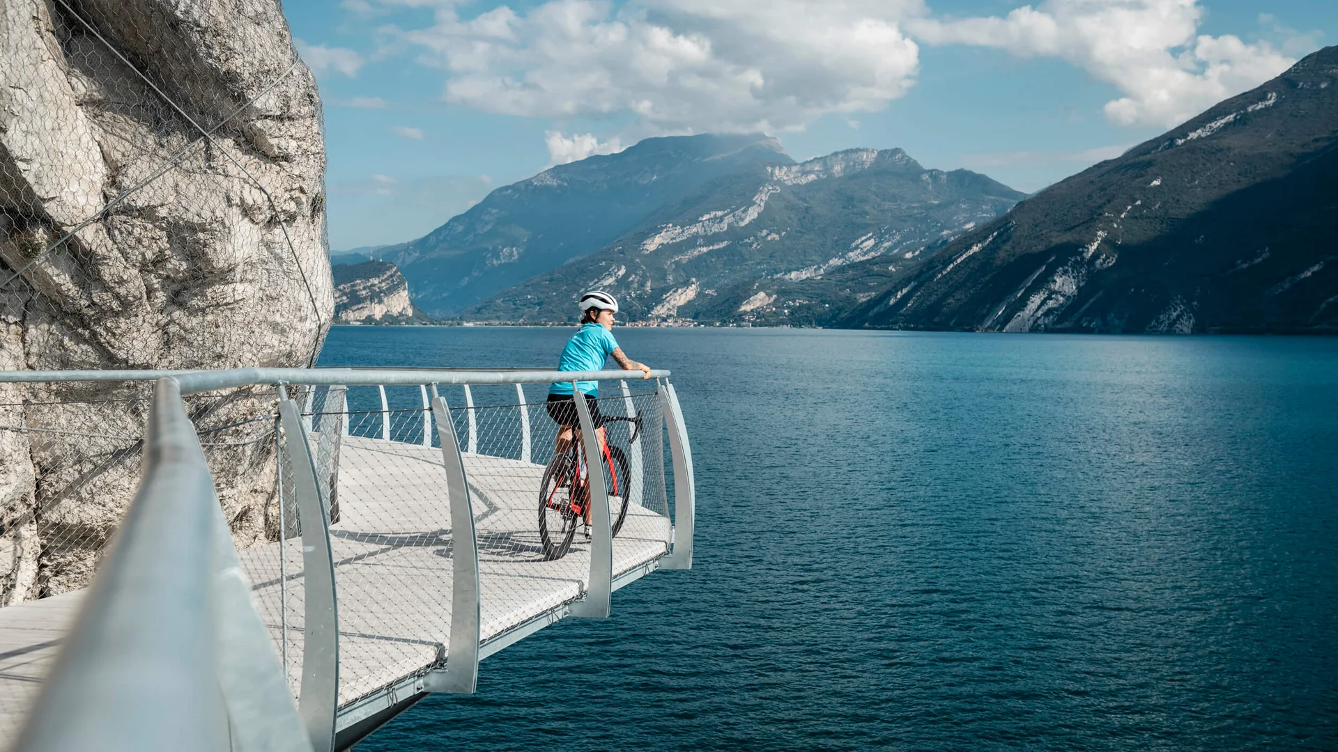Cyclist on a walkway overlooking lake and mountains on a sunny day
