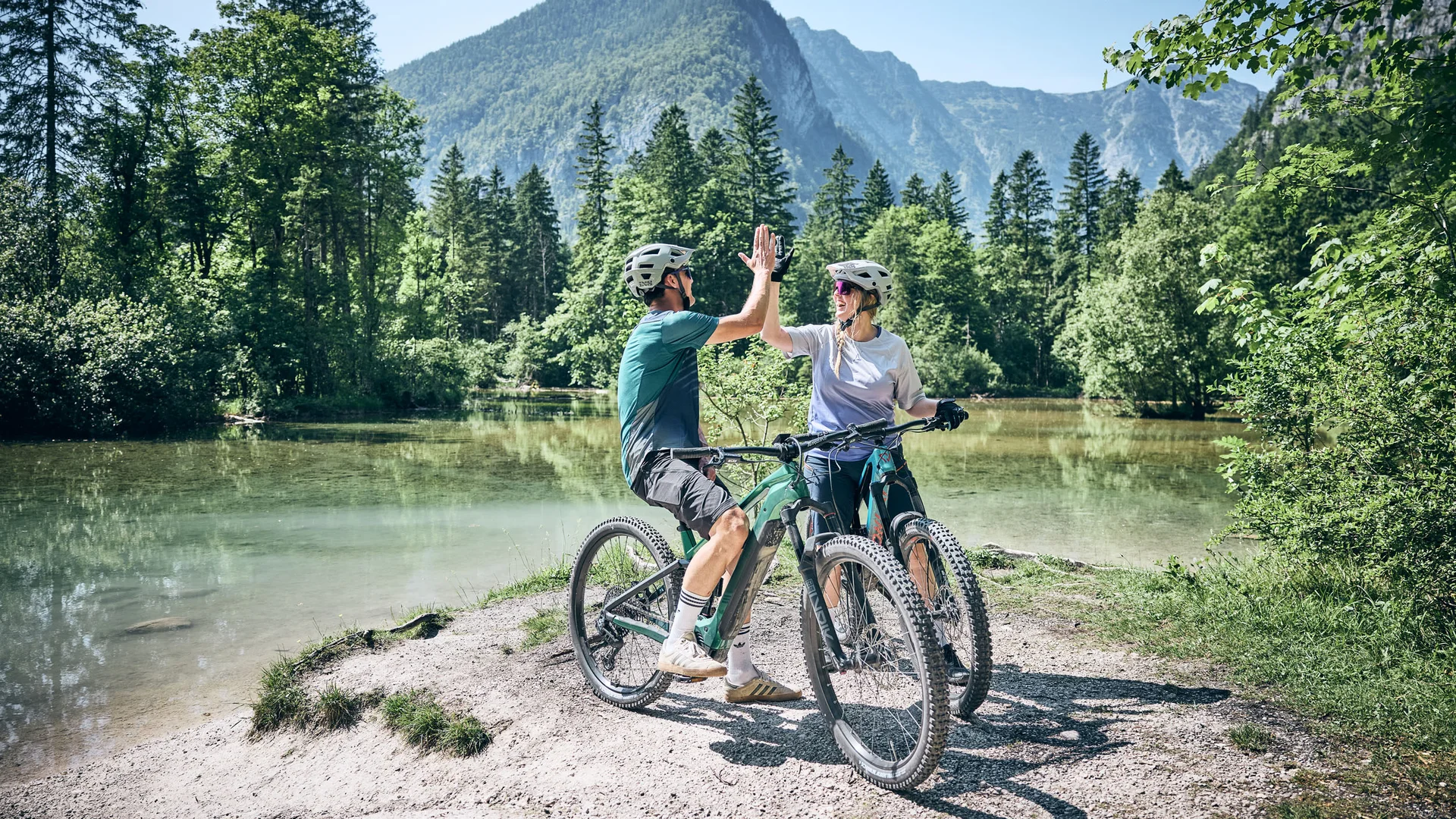 Brands © Tobias Köhler Two cyclists high-fiving by a mountain lake