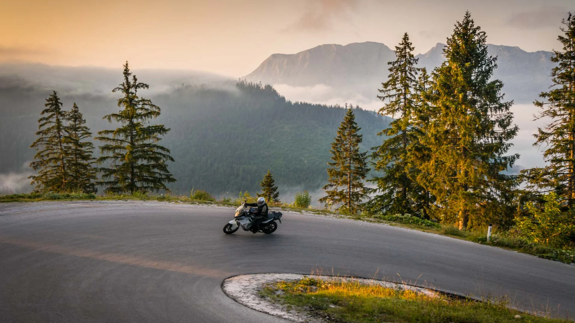 Motorcyclist riding on winding mountain road at sunrise