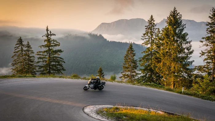 Motorcyclist riding on winding mountain road at sunrise