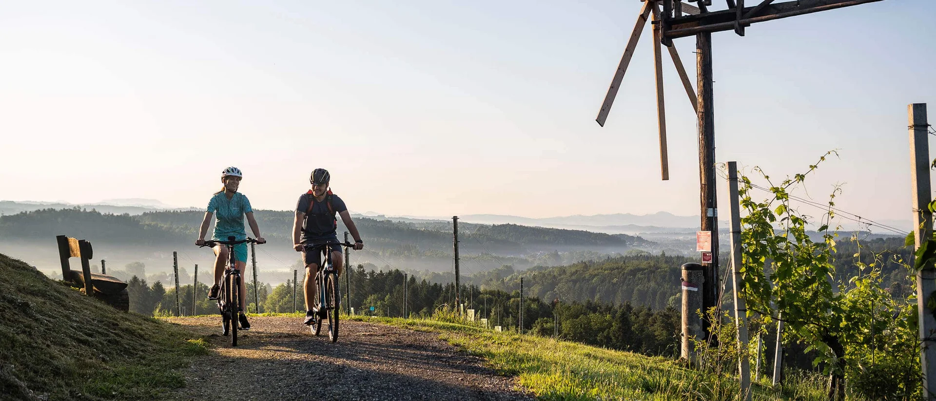 Velontour Two cyclists on a country path with a windmill and hills in the background