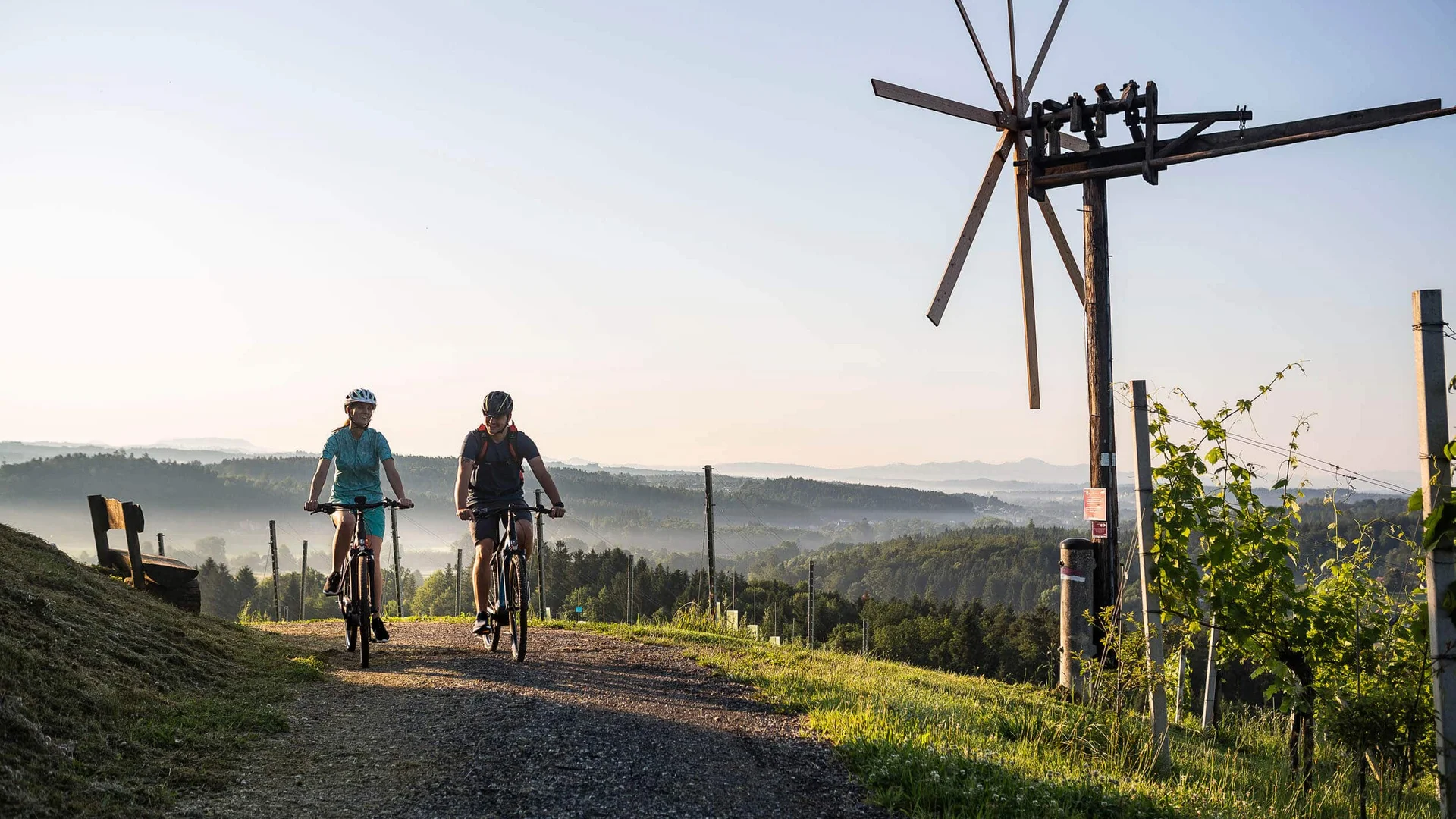 Brands Two cyclists on a country path with a windmill and hills in the background