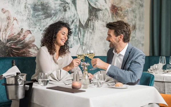 Couple toasting with white wine glasses at a restaurant