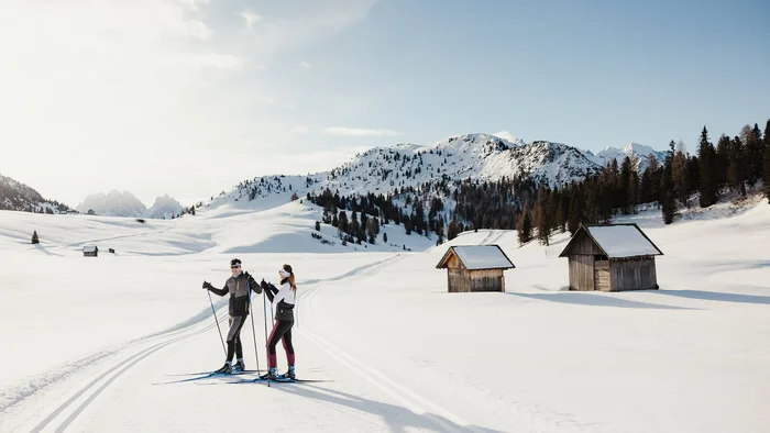 Cross-country skiing & ski touring hotel © Alex Moling Two cross-country skiers on snowy trail near cabins and mountains