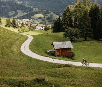 Alta Badia © Alex Moling Zwei Radfahrer auf einem Weg im grünen Tal mit Bergen im Hintergrund