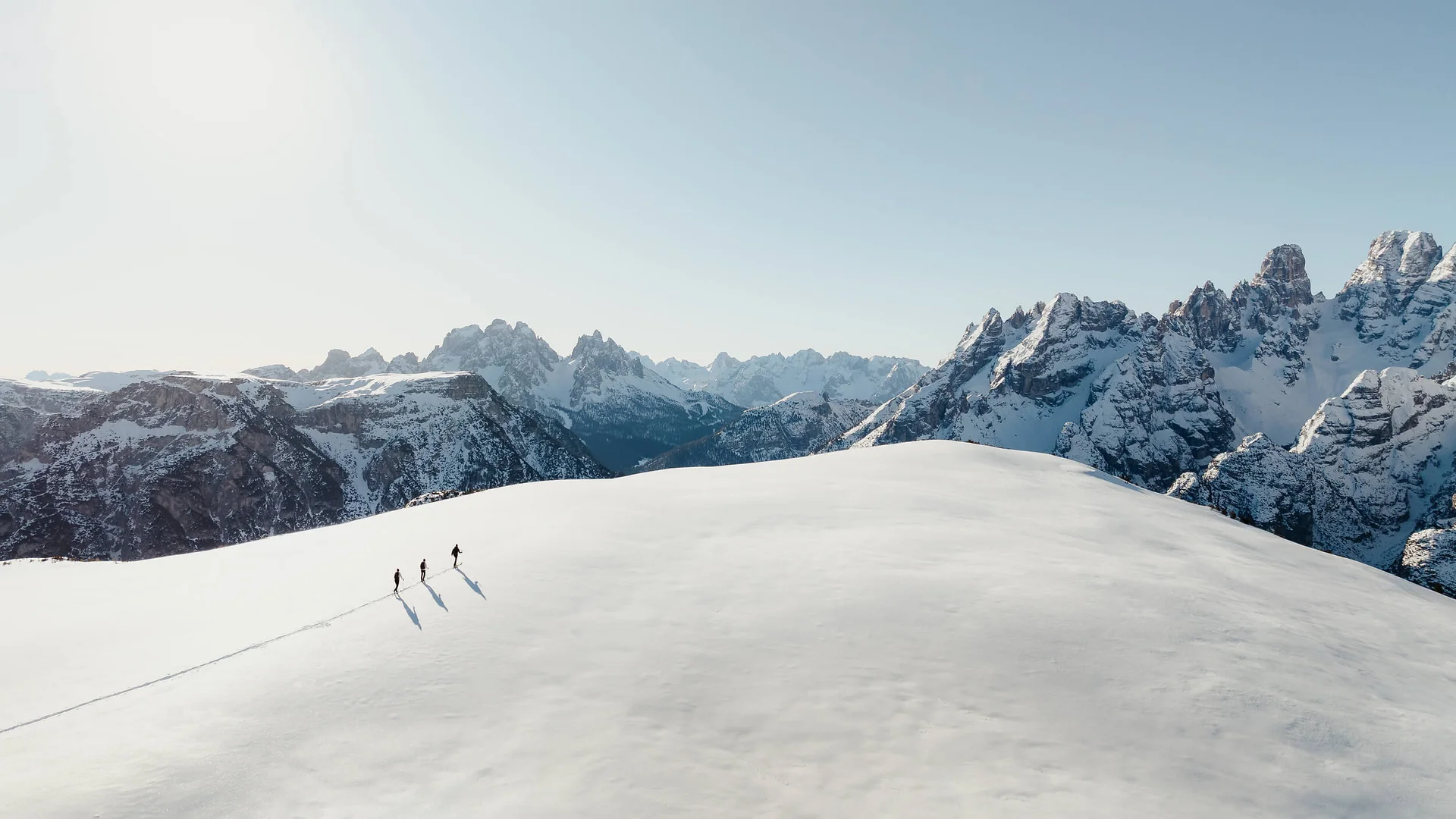 Three hikers walking on a snowy mountain with mountain range in background