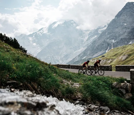 Nauders – Reschensee © Felix Saller Zwei Radfahrer fahren auf Bergstraße mit schneebedeckten Bergen im Hintergrund