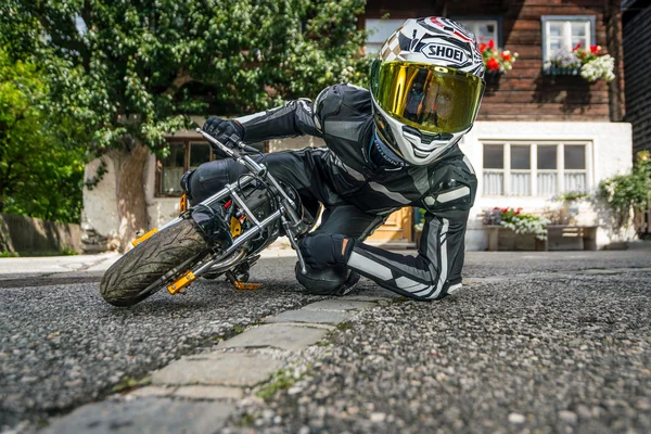 MoHo – Motorbike Hotels © Moppetfoto.de Person in motorcycle gear lying next to small bike on street in front of house