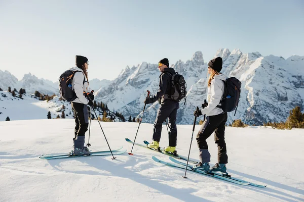 Three skiers standing on snow with mountains in the background