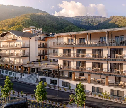 Cristallo Sport & Wellness Hotel © Andrea Acler Modernes Hotelgebäude vor bewaldeten Bergen im Sonnenlicht