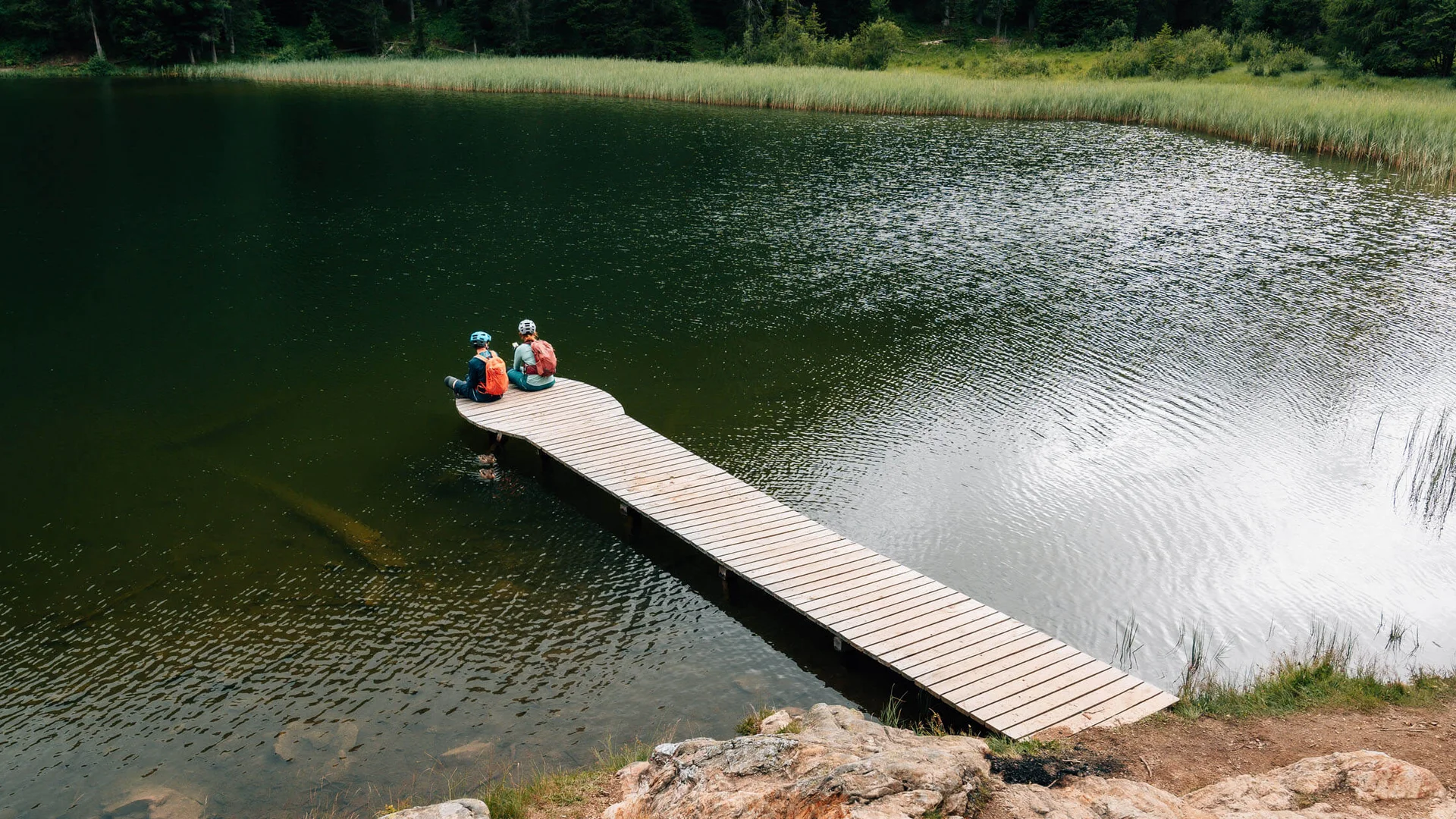 Two cyclists sitting on a wooden pier over a lake in nature