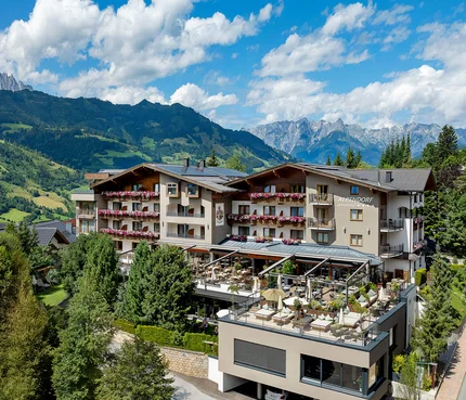 Aktivhotel Alpendorf © Atelier Oczlon Hotel Alpendorf mit Terrasse in bergiger Landschaft bei Sonnenschein