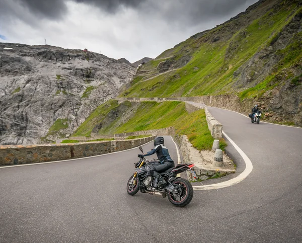 MoHo – Motorbike Hotels © Moppetfoto.de Motorcyclists riding on winding mountain road with rocky cliffs and cloudy sky